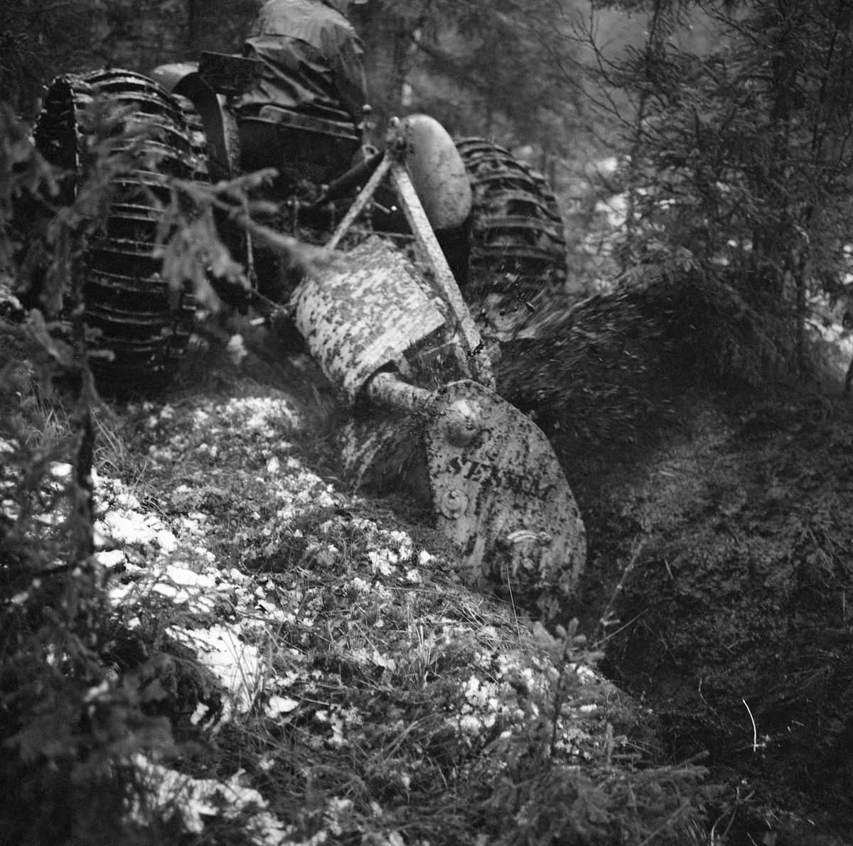 Demonstrasjon av grøfting med traktor og grøftefres under en driftsteknisk orientert skogdag i Strandbygda i Elverum (Hedmark) høsten 1963. Fotografiet viser traktoren og fresen, som var av en type som ble kalt «Sesam», for å poengtere at den kunne gjøre underverker i myr som skulle dreneres. Slike grøftefreser ble brukt til å etablere grunne eller halvdjupe grøfter i myr. Fresen var lagd av stål. Det arbeidende organet var en skovl (rotor) med diameter på cirka 70 centimeter, og med tre utskiftbare kniver. Fresen kunne kjøres med to hastigheter. Den arbeidet vinkelrett på grøftenes lengderetning og trekkraftas fartsretning. Massen ble kastet mot ei av sidene. Under ideelle forhold kunne denne maskinen opparbeide om lag 1 000 meter 30 centimeter djup grøft i løpet av en time. Grøftefresen måtte ofte kjøres to ganger i samme trasé for å etablere ei god grøft med dybde på opptil 50 centimeter. Grøftefresen kunne ikke brukes i myr der skovlknivene kunne treffe stein eller røtter.