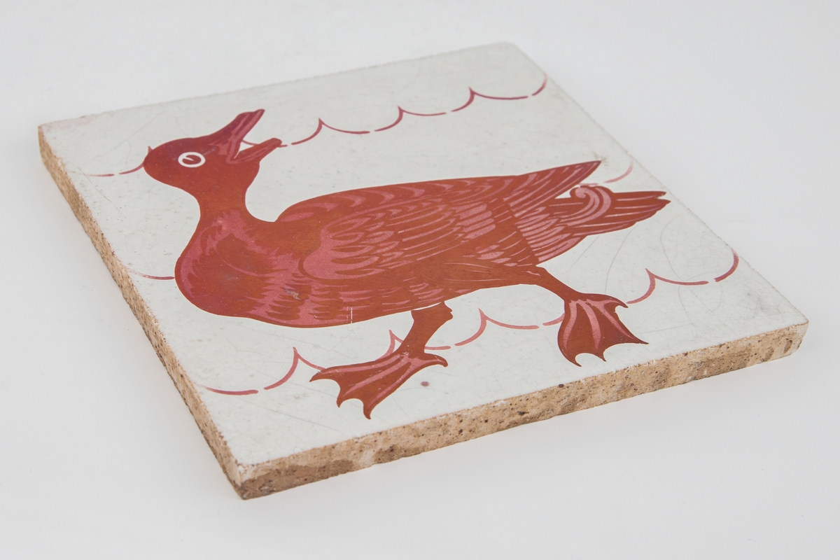 Flis med dyremotiv i rød lusterglasur som avbilder en and.