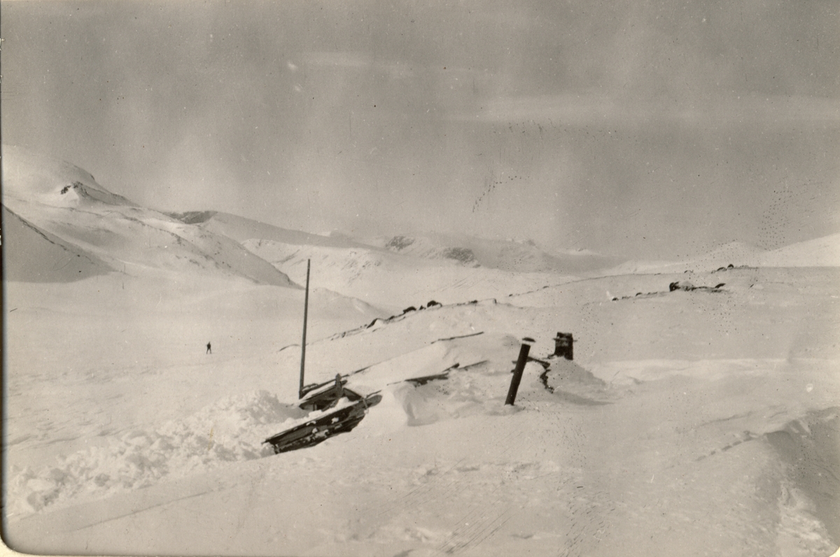 Den gamle bua ved hytta Russboden ved Russvatnet er helt nedsnødd. Til venstre skimtes en skigåer. Fotografert påsken 1910.