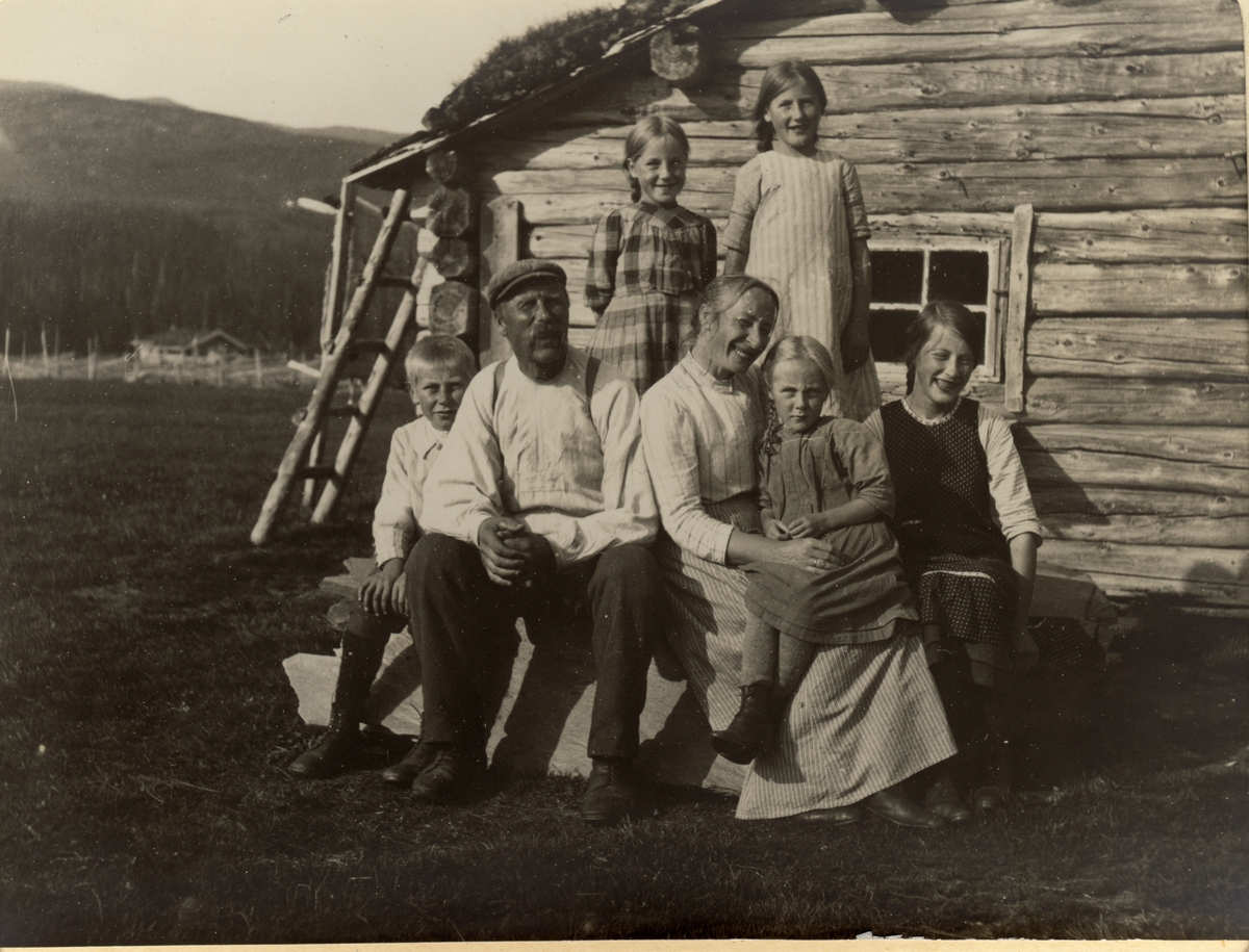 Ola Fosmoen (Dram Ola)med familien ved familiens tømmerhus i Fjergen i Trøndelag. Ola Fosmoen var antagelig husmann/vaktmester hos Fearnley-familien. Fotografert 1913.