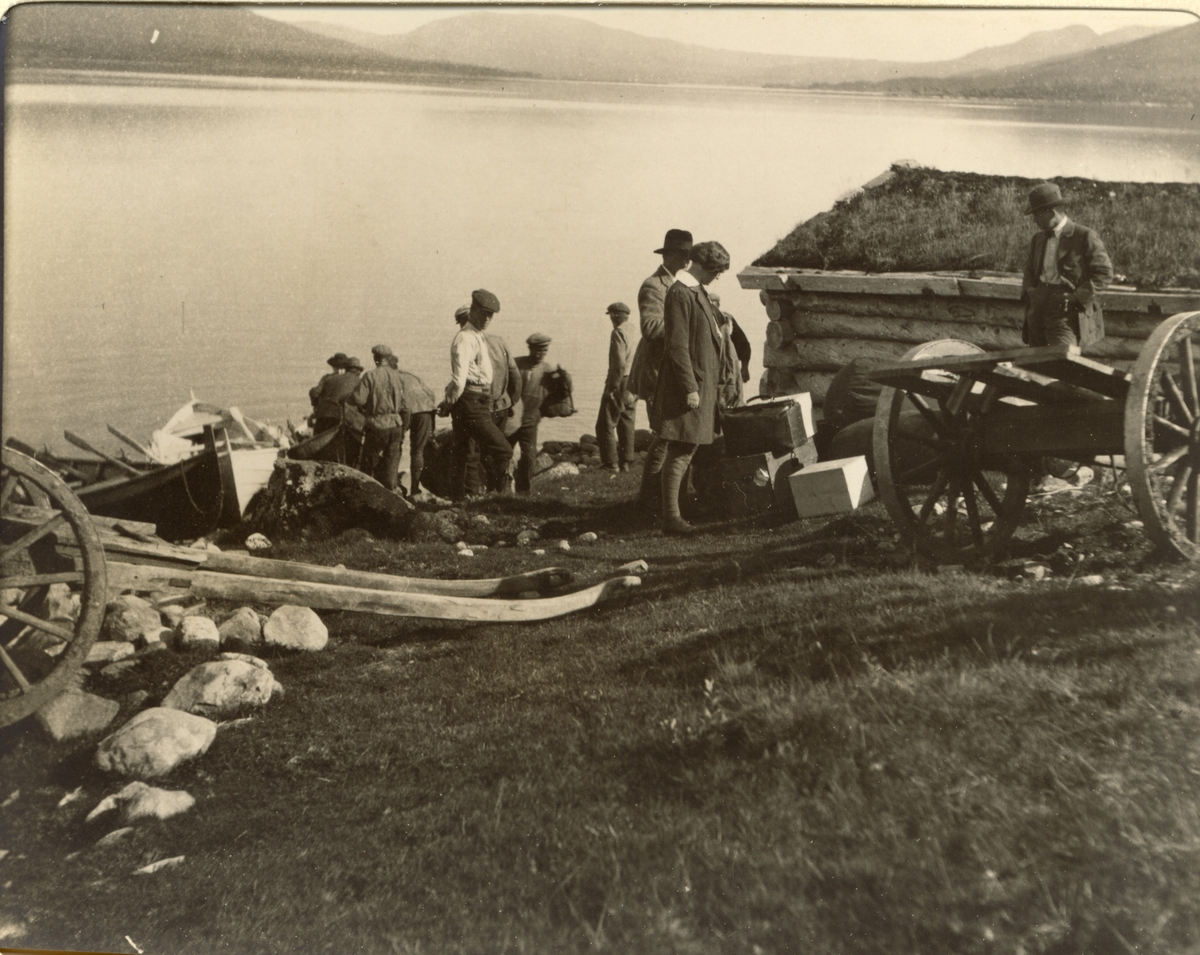 Jegere og medhjelpere ankommer vestenden av Fjergen etter båtreise fra jakthytte i østenden. Trekkvogner til bagasje står klare. Fotografert 1913.