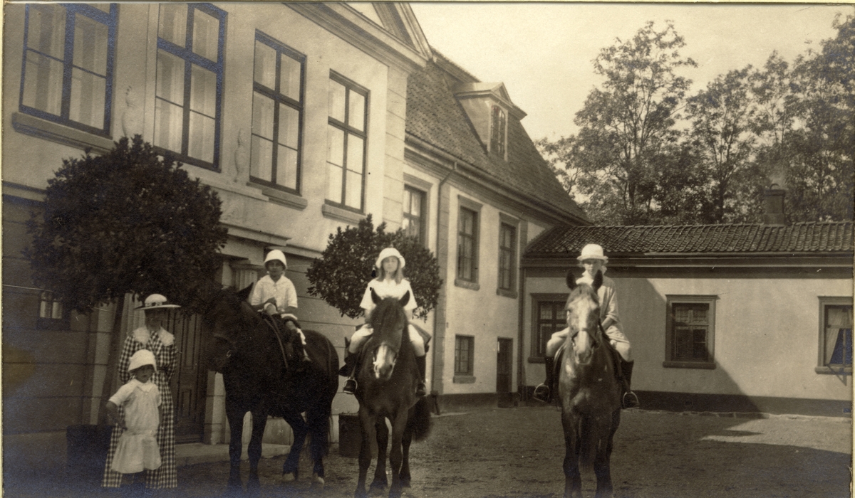Nini Egeberg og datteren Karen står ved inngangspartiet til Bogstad gård, men jentene Lucy Egeberg, Mimi Egeberg og Johanne Løvenskiold sitter på hver sin hest. Fotografert 1918.