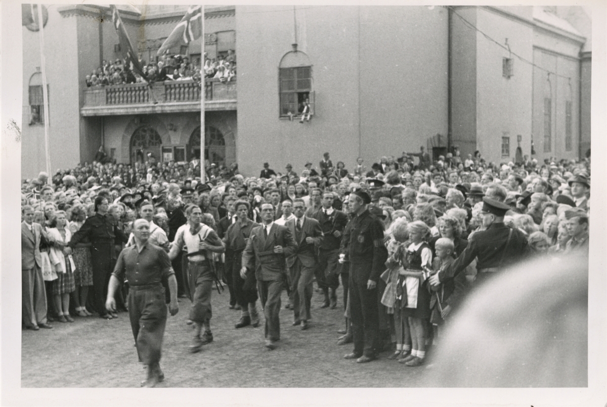 Motstandsfolk fra hjemmestyrken går i parade opp til Rådhuset den 29. juli for å gjøre ære på Kronprins Olav. Og Kronprinsen fikk hilset sine landsmenn sa de marsjerte forbi podiet på Rådhuset i Haugesund.