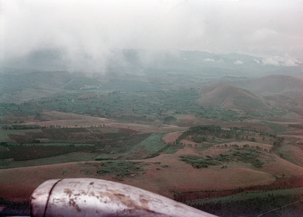 Flygbild över naturlandskap i Kongo tagen under Kongokrisen, 1963. Berg vid horisonten. Med flygplansmotor synlig.