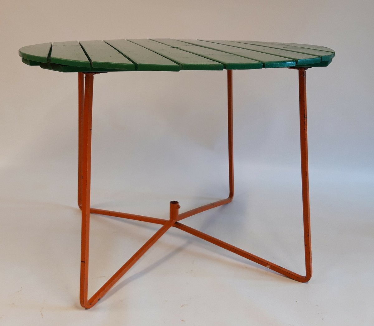 Ett rundt bord med 10 grønnmalte planker som bordplate. Understell av oransjemalt metall. Hull og feste for parasoll.  Stolene er laget av fjærstål som gir mulighet for svikt.