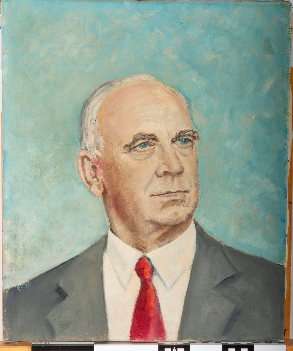 Portrett, Brystbilde, trekvart profil vendt mot høyre. Kledd i hvit skjorte, rødt slips og grå jakke. Blålig bakgrunn.