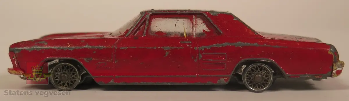 Hovedsakelig rød og sekundært svart Buick modell. Den er laget av metall og mangler alle dekkene. Skala 1:57.
