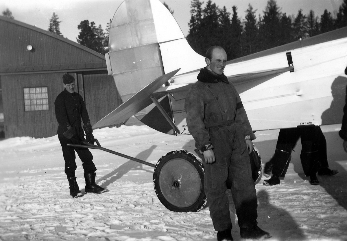 Flytt av flygplan S 6, vintertid. Vid stjärtpartet styr en mekaniker flygplanet. Framför planet står en man i flygoverall. 1930-tal.