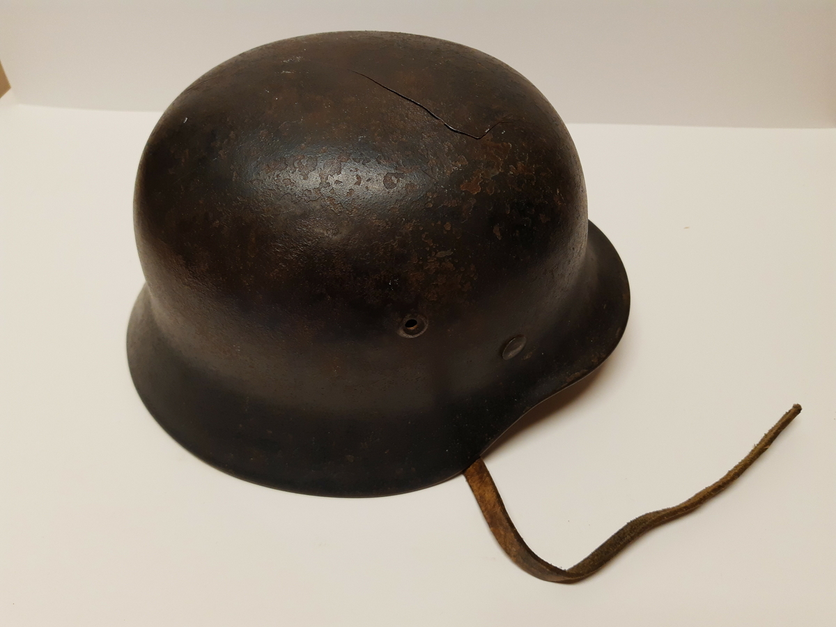 Stålhjelm av typen brukt av tyske soldater under 2. verdenskrig. Hjelmen har rem med spenne til å feste under haken. På venstre side er hjelmen dekorert med riksvåpenet til det tredje riket, ørnen over et hakekors. Merket er veldig slitt.