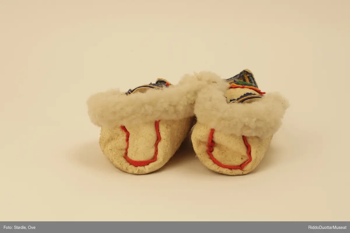Tøfler av saueskinn sydd etter mal av tradisjonelle samiske skaller. Skinnet er vrangsydd med ulla inn, unntatt  brettekant som har har ulla ut.  Sømmene rundt overlær og helkappen har biser i ullklede. 