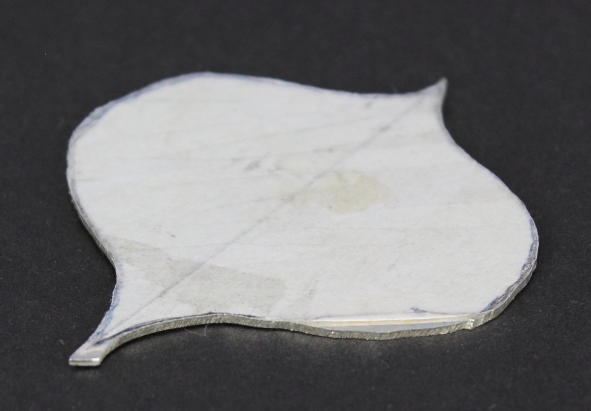 Silverplåt i spaderform med papper pålimmat på ena sidan. Den andra sidan lätt oxiderad.