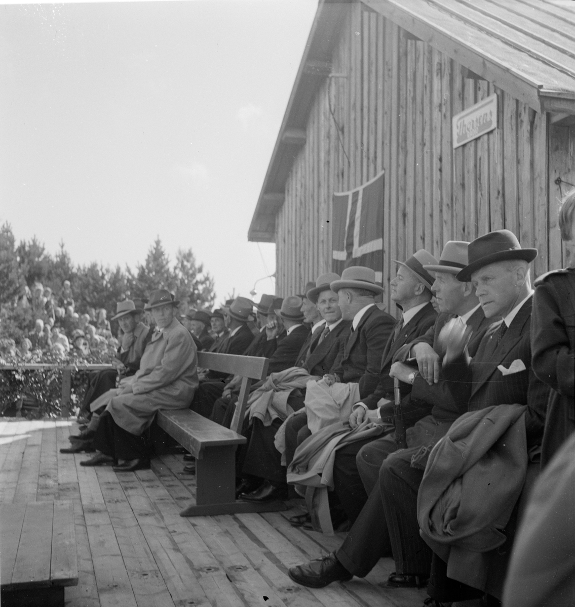 Menn sitter på rad og rekke bak talerstolen under åpningen av Eigerøy bru.