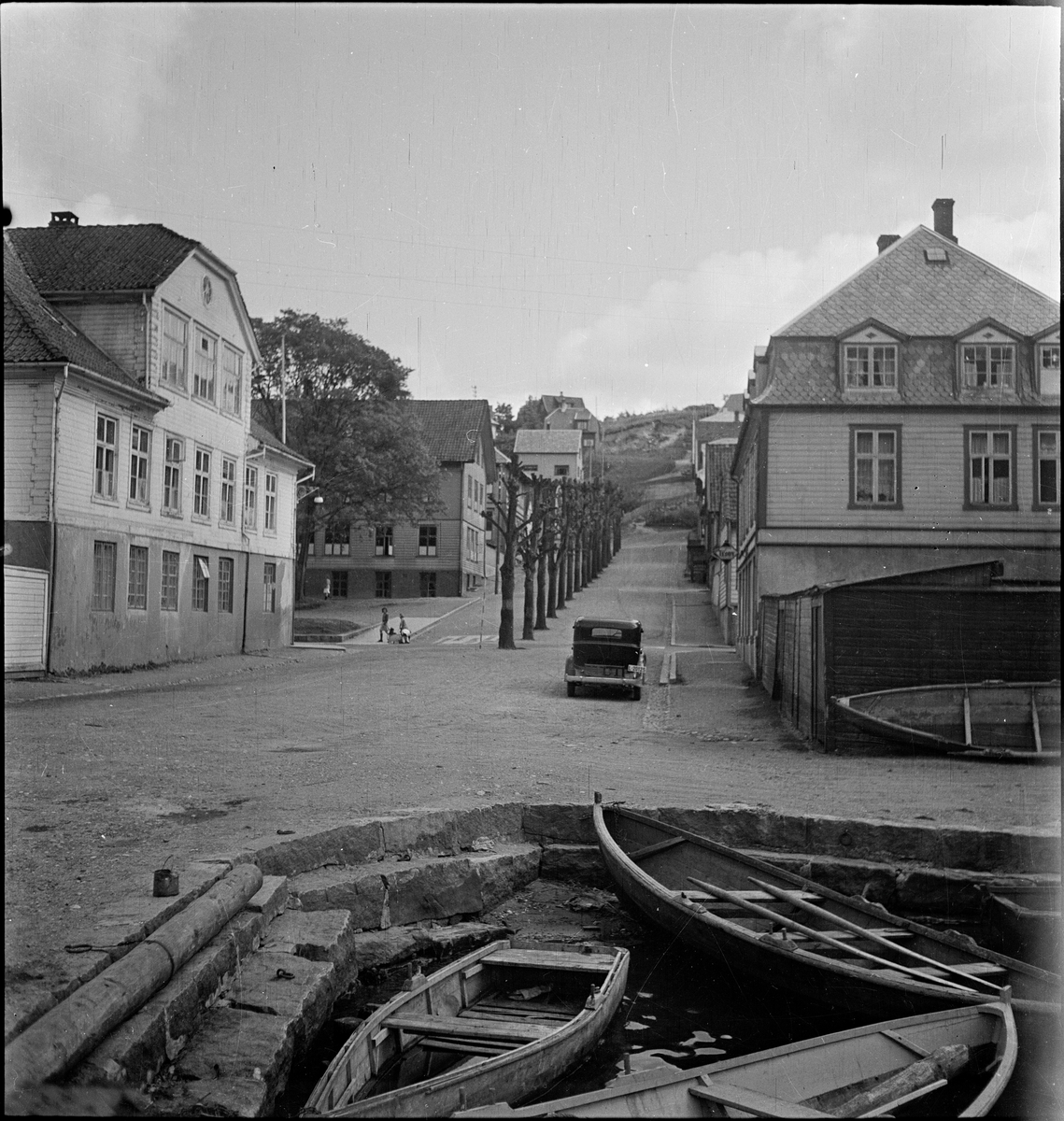 Robåter ved Skriverbrygga i Egersund. Skriveralmenningen med alléen går oppover fra kaien. Strandgaten nr. 58 ligger på venstre side, og nr. 56 på høyre side.