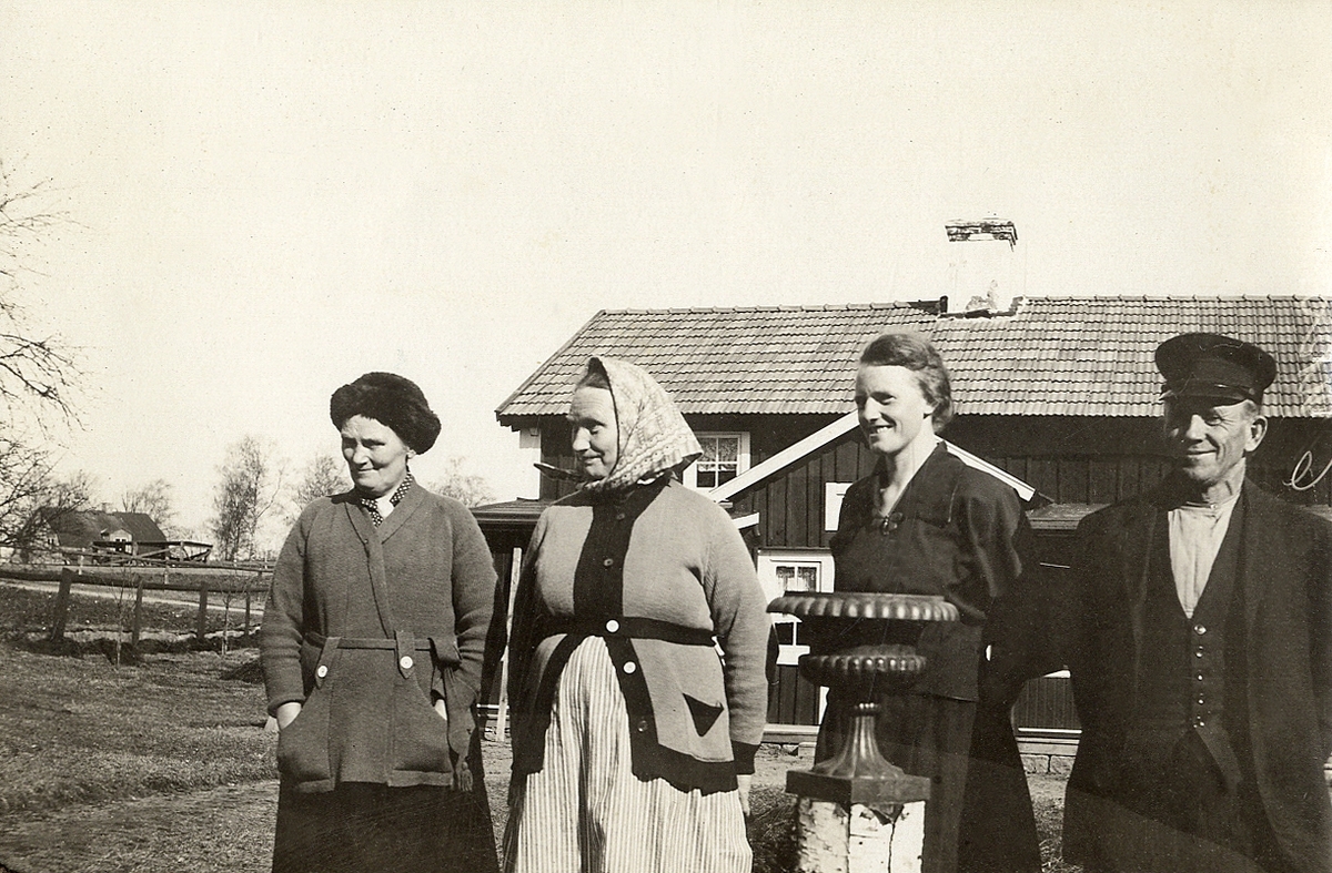 Tre kvinnor och en man står framför ett bostadshus på landet.