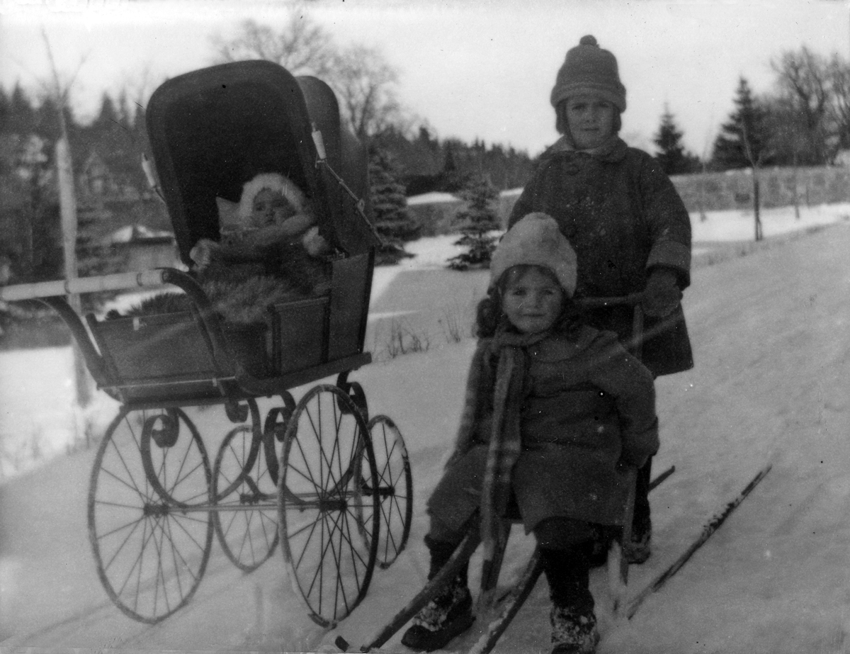 Två barn på en spark bredvid en barnvagn med en bebis.