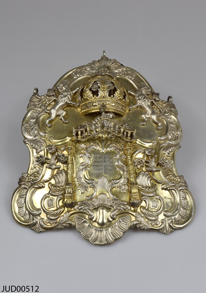 Torahsköld tillverkad av silver. Skölden är delvis förgylld och är rikligt dekorerad med en tredimensionell krona flankerad av lejon. Blommor och djur, samt ristad hebreisk text.
