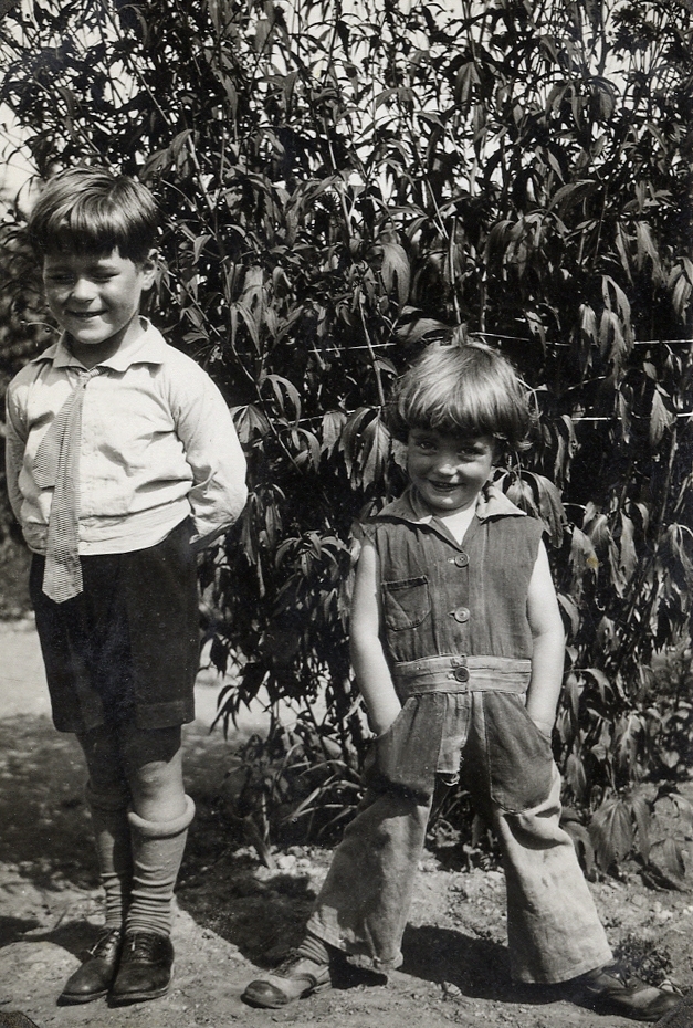 Två små pojkar poserar för fotografen, i en trädgård.