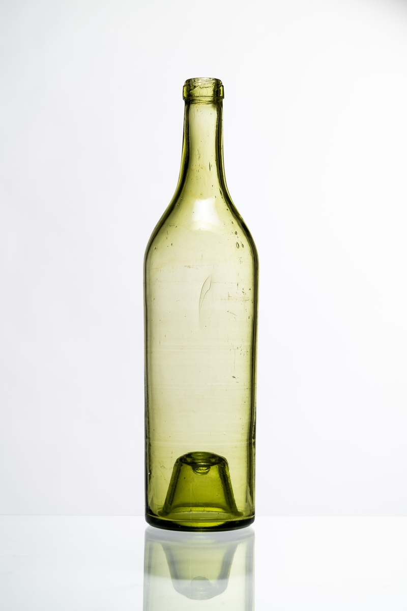 Butelj för brännvin av ljust grönt glas, avsedd för tillslutning med naturkork. Buteljen har "Kinnekullebotten" med liten kula. Blåsor i glaset. Hantverksmässigt tillverkad vid Sunds glasbruk, Jönköpings län. Se vidare Historik.