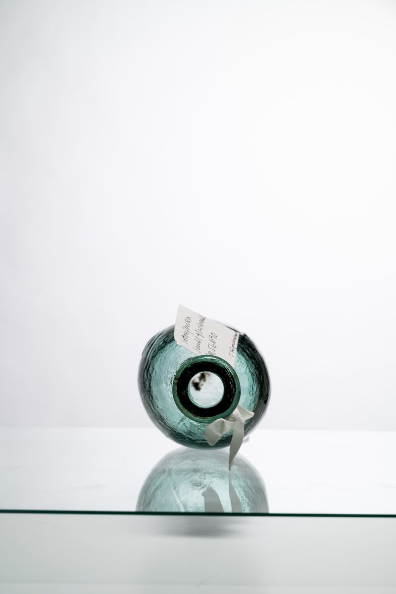 Flaska för vatten av ljust grönt glas, med oval, liggande form. Märkning i relief: "SODA". Flaskan gjordes med liggande form för att naturkorken inte skulle torka. Tillslutande kork saknas. Hantverksmässigt tillverkad vid Sunds glasbruk, Jönköpings län. Se vidare Historik.