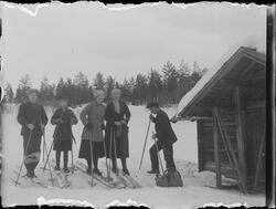 To menn, to kvinner og en jente stående ved hytte med ski på