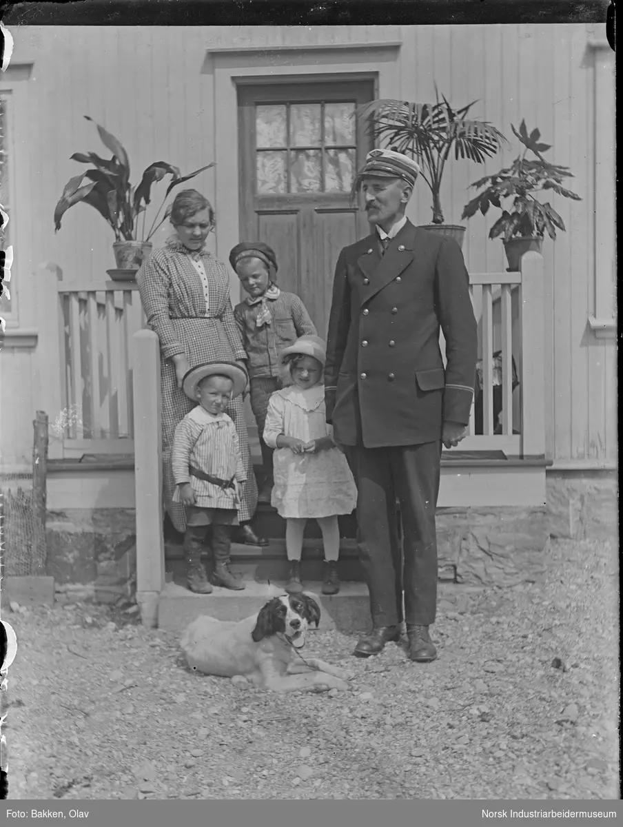 Ramilien Rasmussen stående utenfor stasjonsmesterboligen på Gransherad stasjon. Stasjonsmester Sigurd Rasmussen i uniform. Hund liggende på bakken foran familien.