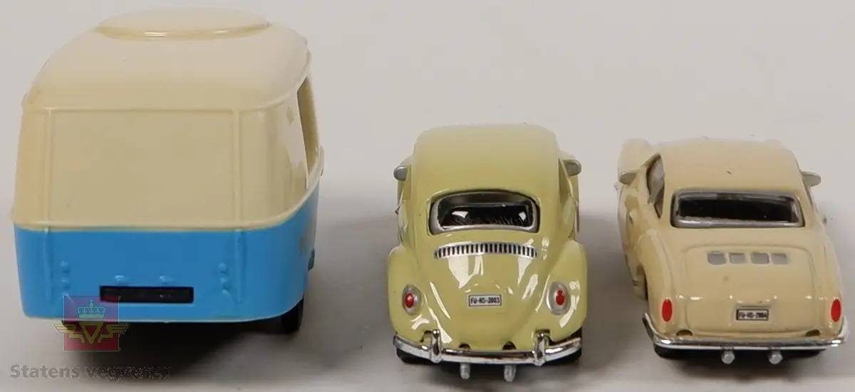 Tre miniatyrmodeller. En Volkswagen Beetle, en Volkswagen Karmann Ghia og en campingvogn. Begge bilene er i farge beige, og campingvognen er blå og beige. Bilene er laget i metall, og campingvognen er laget av plast.