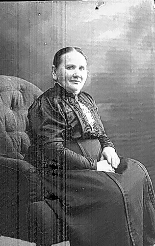 Porträtt av en kvinna som sitter i en fåtölj med händerna i knät.