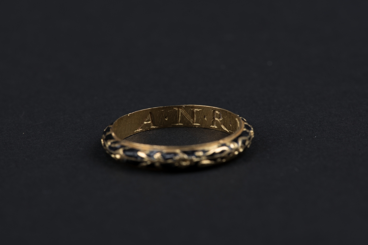 Fingerring av guld med inlagd svart emalj. 
Ringens insida har ingraverade initialer, som indikerar att ringen använts som förlovningsring.