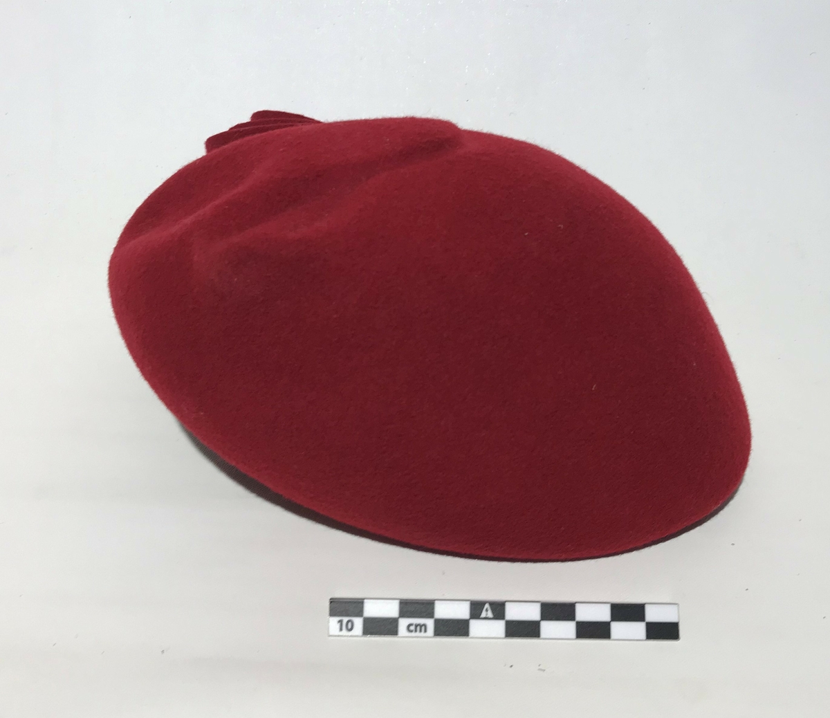 Hatt. Rød damehatt i ullfilt med en stor pin til pynt. Hatten har strikk til å ha under haken.
