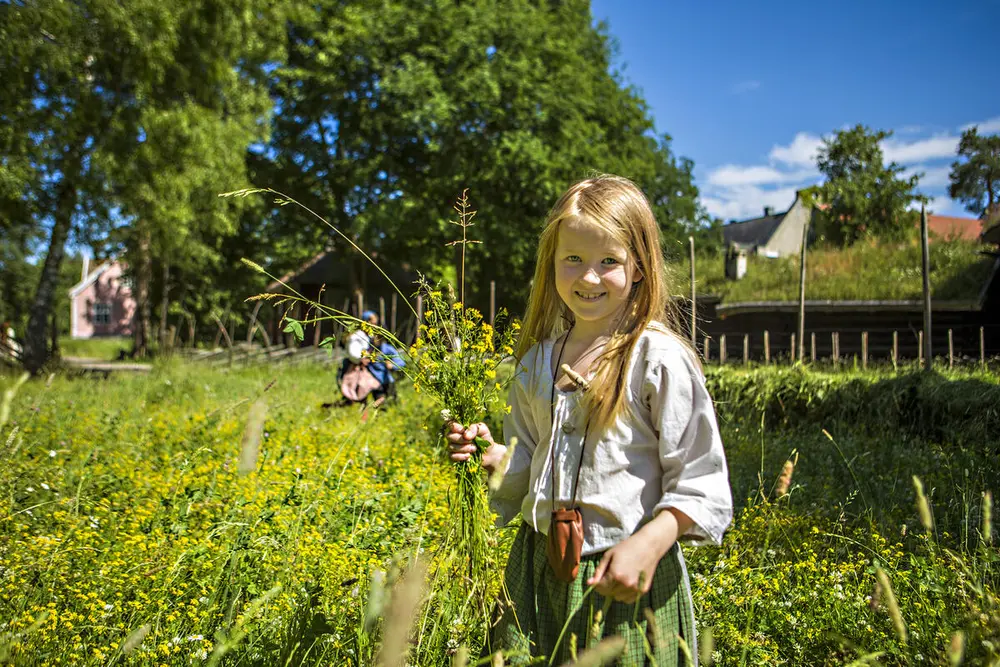 En jente står i en bomstereng med en blomsterbukett i hånden