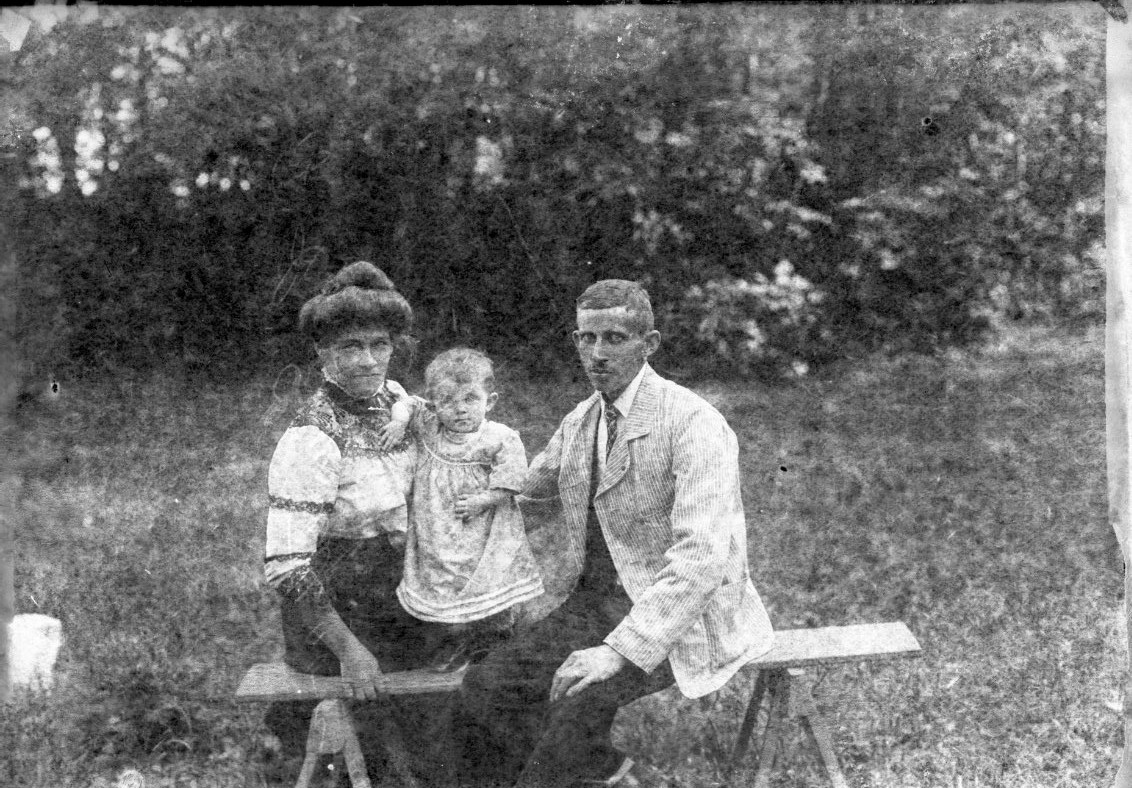 En man och en kvinna sitter med ett litet barn mellan sig på en bänk på en gräsmatta. Sannolikt i närheten av Visingsborgs slottsruin. Det är sommar.