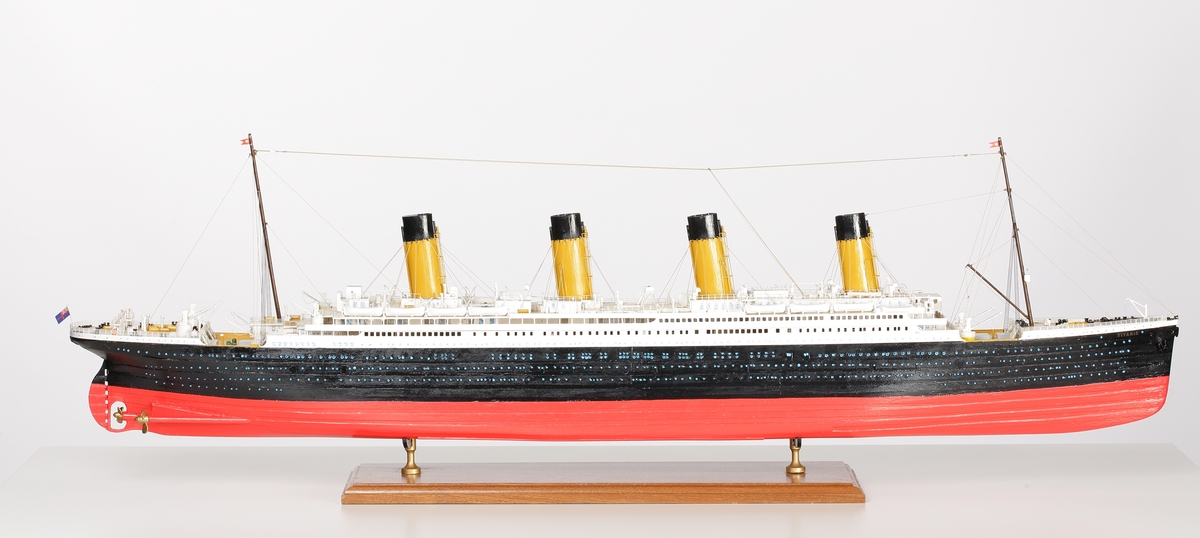 Oceanångare (Titanic) i trä och textil. Skrovet är målat i rött, svart och vitt, samt blått som är önsterventilerna. Däcket är trävitt och lackerat. På däcket finns detaljerat all utrustning såsom kranar, livbåtar, hytter, soffor och ventiler. Där finns fyra stora skorstenar med toppar i svart, och två större master med White Star Lines röda vimplar i toppen. Master och skorstenar är förbundna med linor i textil. I aktern är det tre propellrar och ett stort roder under vattenlinjen. Uppe vid relingen finns också en stång med en engelsk statsflagga. Modellen står på en brunbetsad platta i trä.