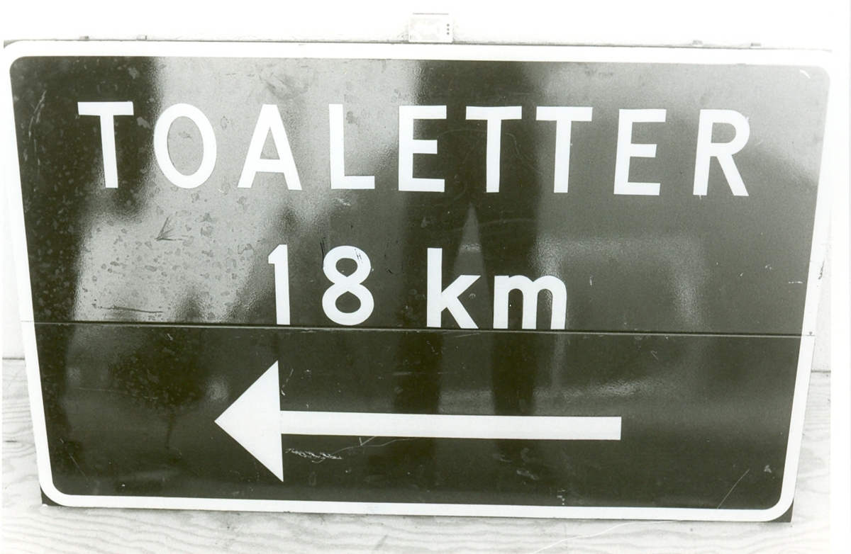 Plåtskylt med blå bakgrund med vit reflextext "TOALETTER 18 km".