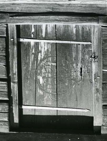 En dörr med två långa metallbeslag sitter i en timmerbyggnad.