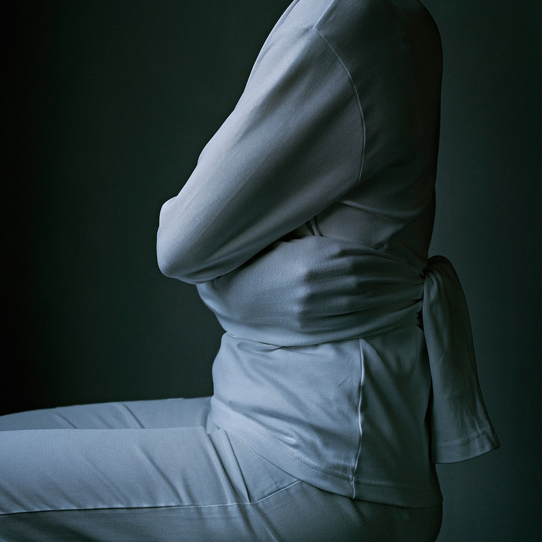 Fotografi i gråskala av kvinna sittandes med tröjans ärmar knutna bakom ryggen likt en tvångströja. Avbildad från axlar till lår.