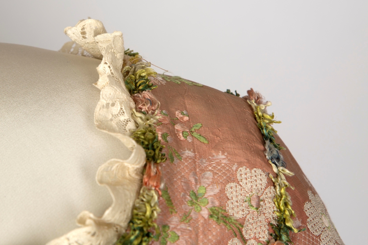 Overkjole av silkebrokade med tilhørende skjørt av samme materiale, begge prydet med blomsterranker av possement. Watteau-folder. Se undernummer.