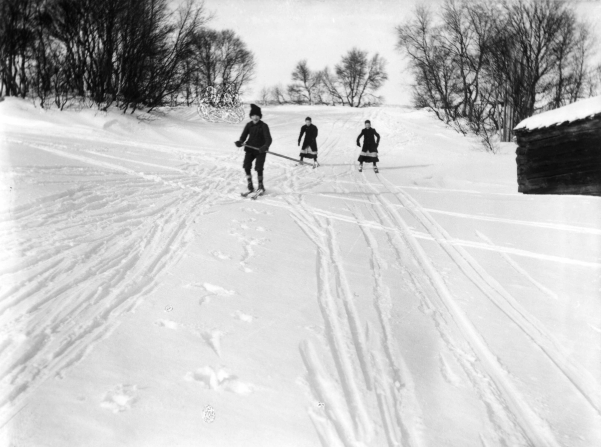 En ung gutt og to unge jenter står på ski ned en bakke