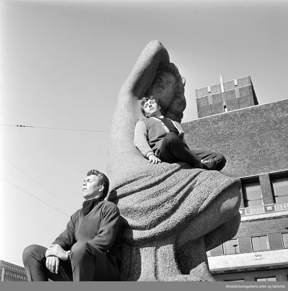 Vårstemning på Rådhusplassen i Oslo. To menn soler seg på Emil Lies skulptur av sittende kvinne, reist 1954-58. 24. April 1962.