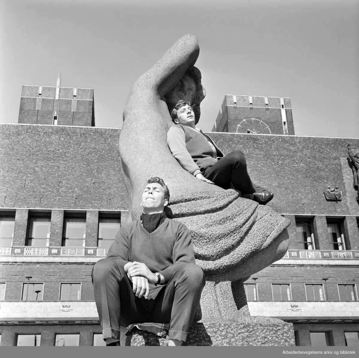 Vårstemning på Rådhusplassen i Oslo. To menn soler seg på Emil Lies skulptur av sittende kvinne, reist 1954-58. 24. April 1962.