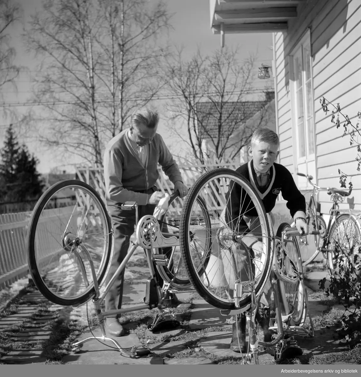 Far og sønn foretar vårens sykkelpuss. Villastrøk i Oslo-området. April 1958.