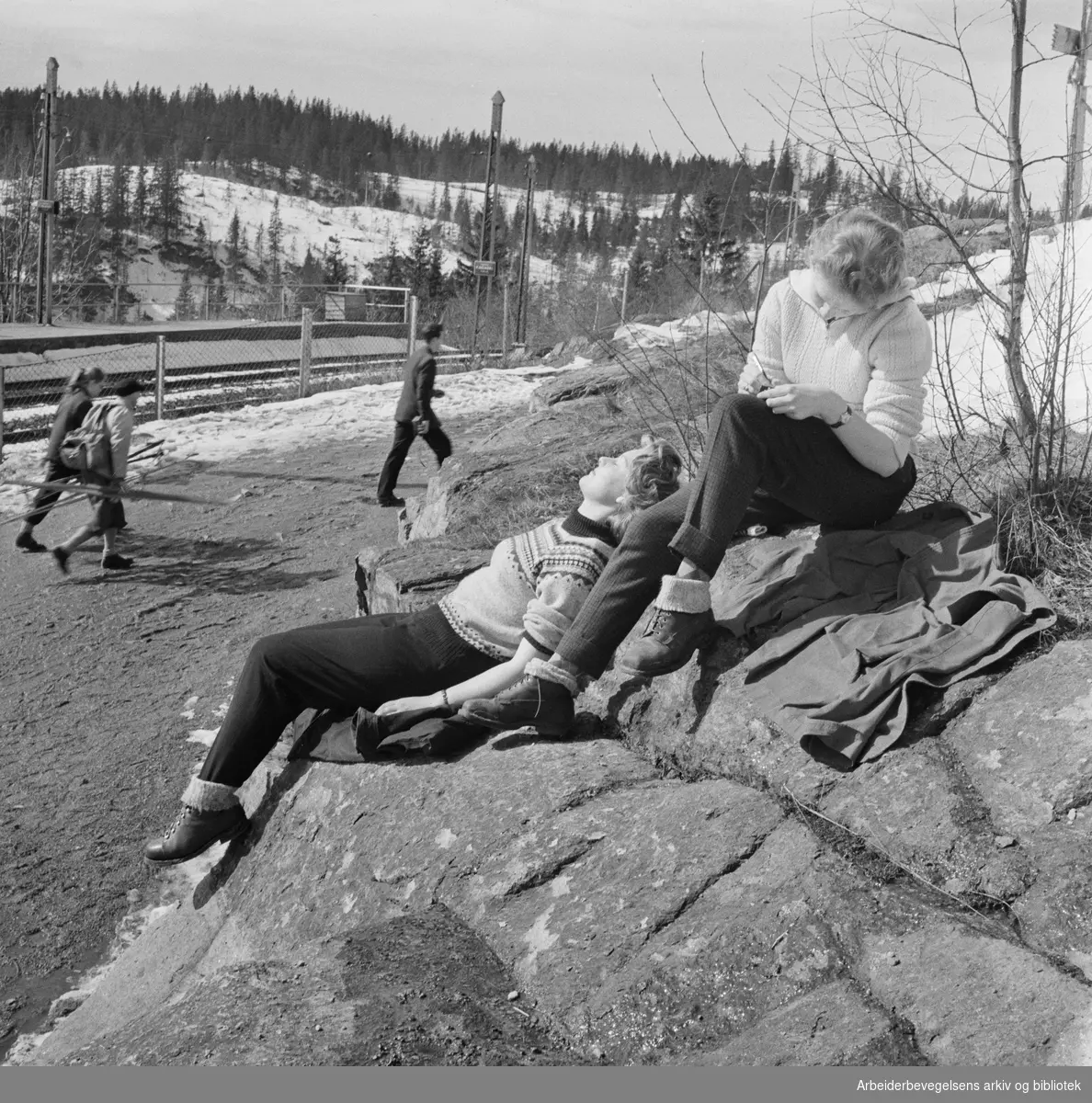 To jenter nyter vårsola på Frognerseteren stasjon. Holmenkollbanen. April 1958.