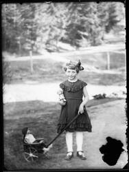 En lita jente med kjole og sløyfe i håret, står og holder ei