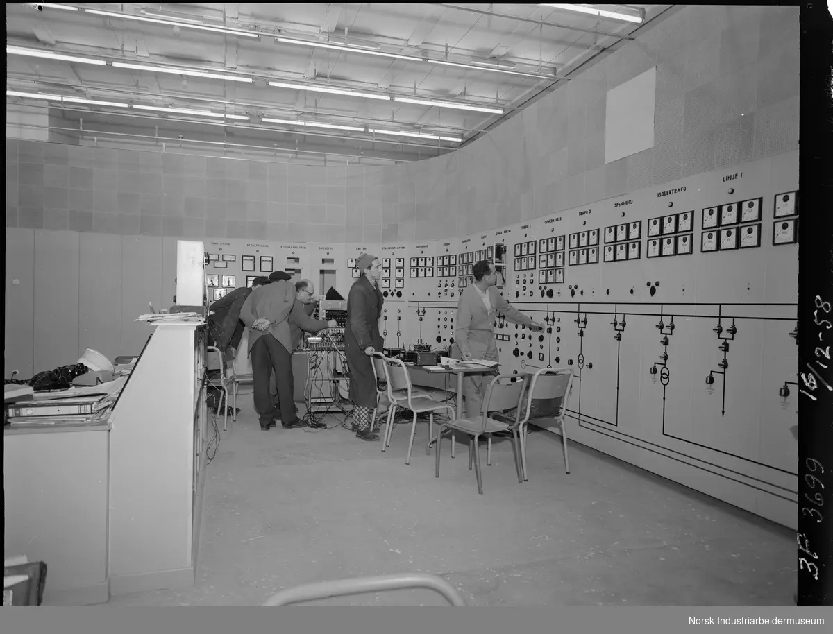 Svælgfos 3 (Svelgfoss 3) Mennesker stående i kontrollrommet. Kontrollpult stående midt på gulvet. Bord og stoler foran kontrolltavlen.