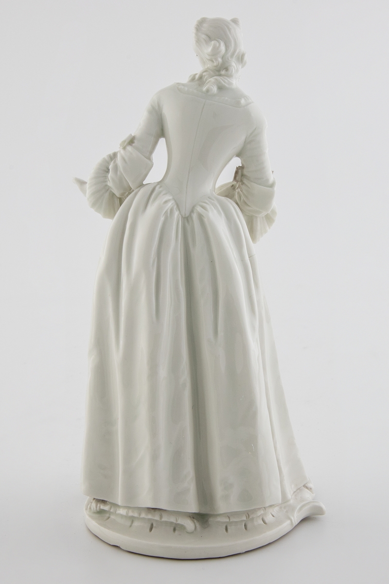 Hvitglasert, umalt porselensfigur av en stående kvinne i 1700-talls klær med uttrykksfull ansiktsmimikk. Kvinnen gjør en avvisende bevegelse mot venstre, med overkroppen lett foroverbøyd. Figuren identifiseres som Isabella, en rolleskikkelse fra comedia dell´arte.