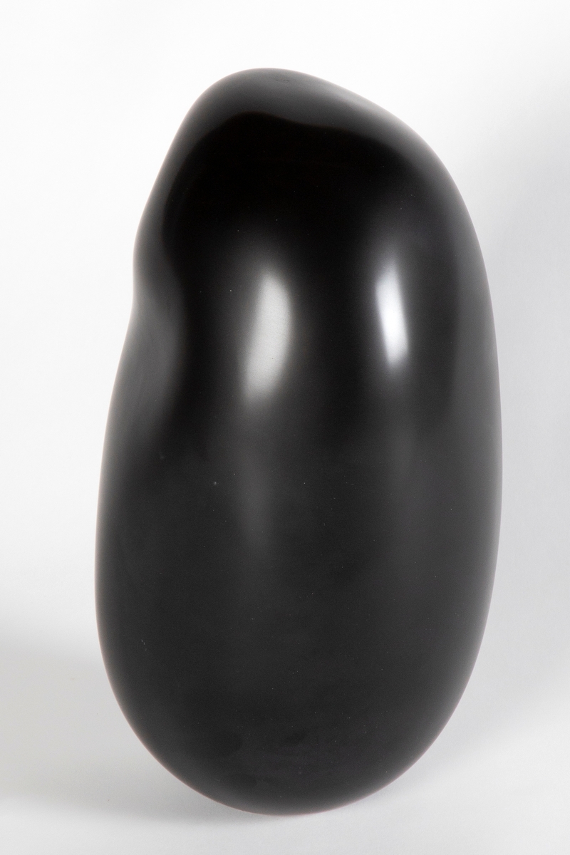 Sort avlang bønneformet glasskuptur. Organisk utforming med halvmat overflate. Mettet sortfarge.