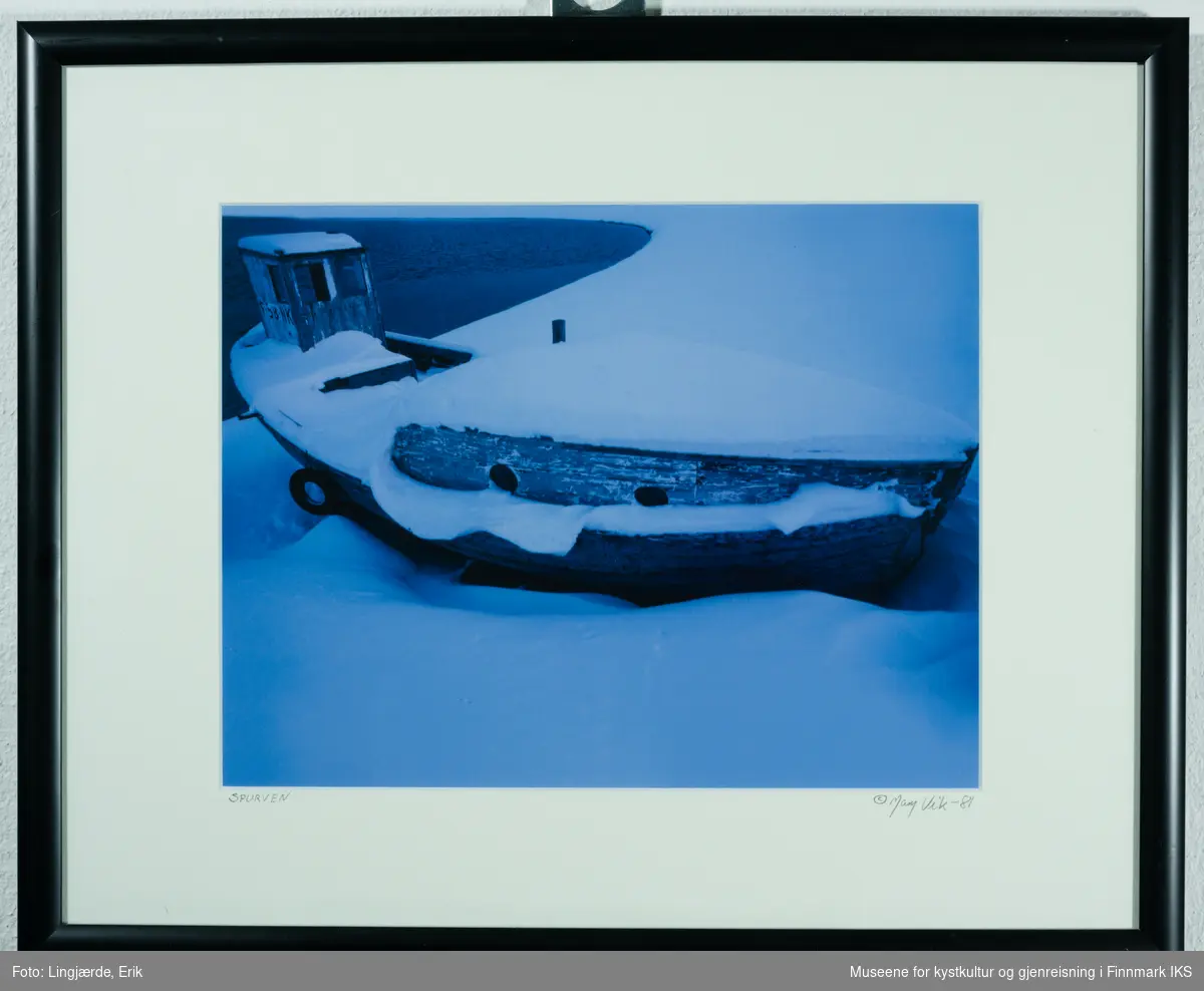 Gammel båt satt på land og dekket med snø. Hele motivet er hovedsakelig i blå og hvit-nyanser.