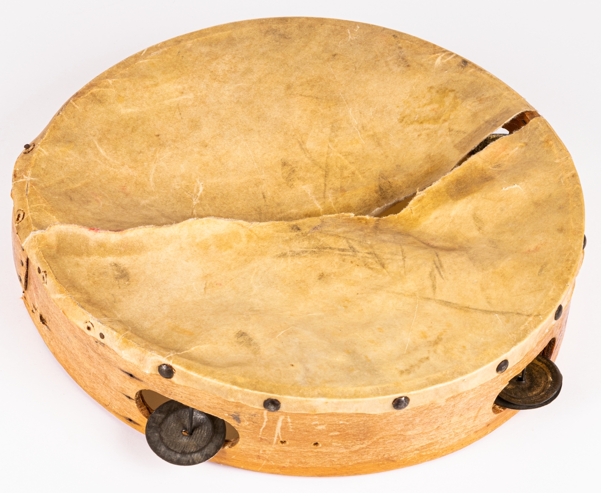 Tamburin med ram av trä, klädd med skinn. Skinnet trasigt. Försett med 4 par mässingscymbaler.