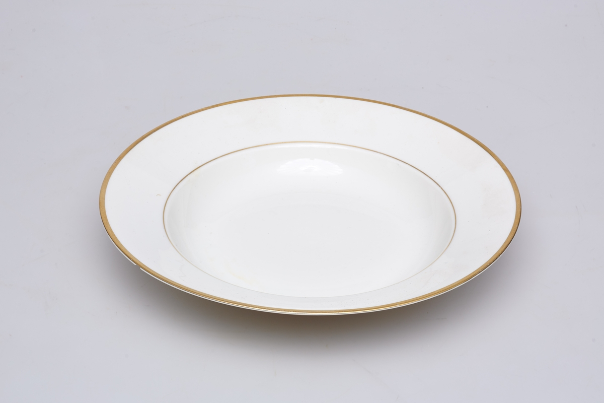 Suppetallerken i hvit porselen. Produsert av Porsgrund Porselen i 1959. Dekorert med gullkant og ring av gull i overgangen til mansjetten. 