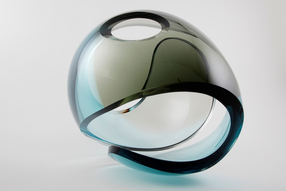 Ovalformet gjennombrutt skulptur i klart og farget glass. De blå og grå partiene overlapper delvis med hverandre, slik at det oppstår en optisk illusjon.