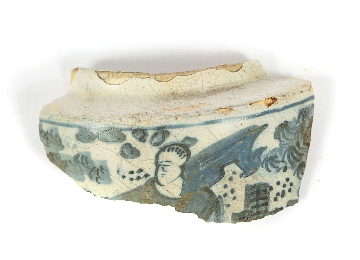 Del av av kruka (del av mynning och skuldra) i holländs fajans med kinesiserande, blå dekor mot vit botten.